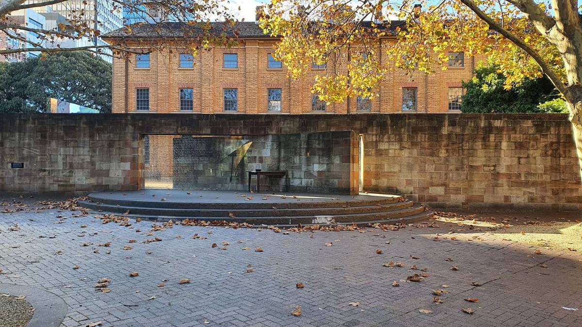 The Australian Monument to the Great Irish Famine at Hyde Park Barracks, a sandstone wall broken by a glazed opening, with autumn leaves on the paving